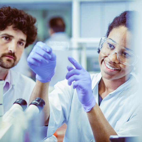 A student veteran works in a laboratory with a colleague, and they are looking at a microscope slide together.