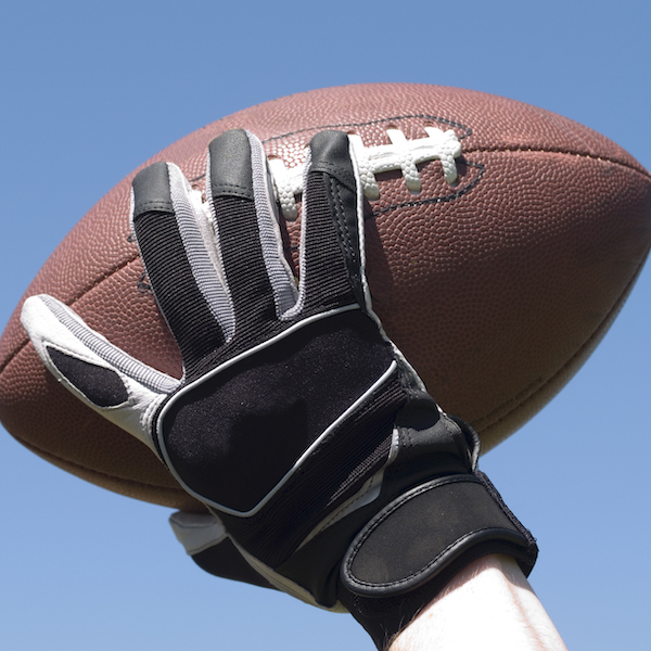 A closely framed image of a quarterback's hand holding a football and nearly ready to throw it